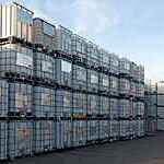 Pallets of metal-framed intermediate bulk containers waiting to be cleaned or recycled in an industrial yard.