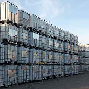 Pallets of metal-framed intermediate bulk containers waiting to be cleaned or recycled in an industrial yard.