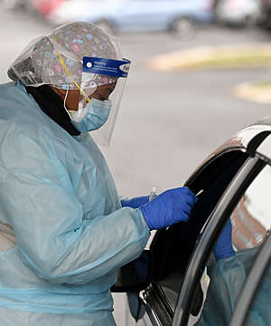 Nurse wearing protective equipment stands by a car window with a nasal swab at a COVID-19 drive-in test station in Reading, PA.