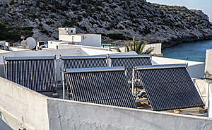 Solar panels for hot water heating stand on the flat rooftop of a house by the sea.