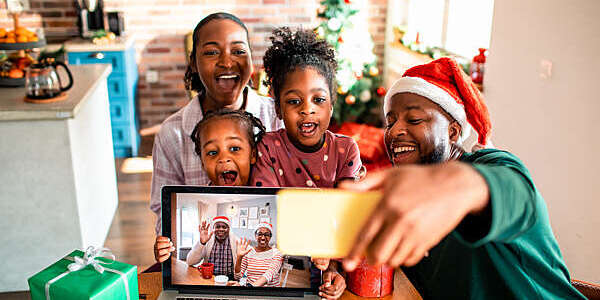 A young family takes a selfie with their grandparents during a video call on their laptop at Christmas time.